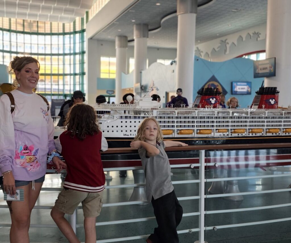 Mom stands with her children at Disney Cruise Line's port entrance with model Disney ship